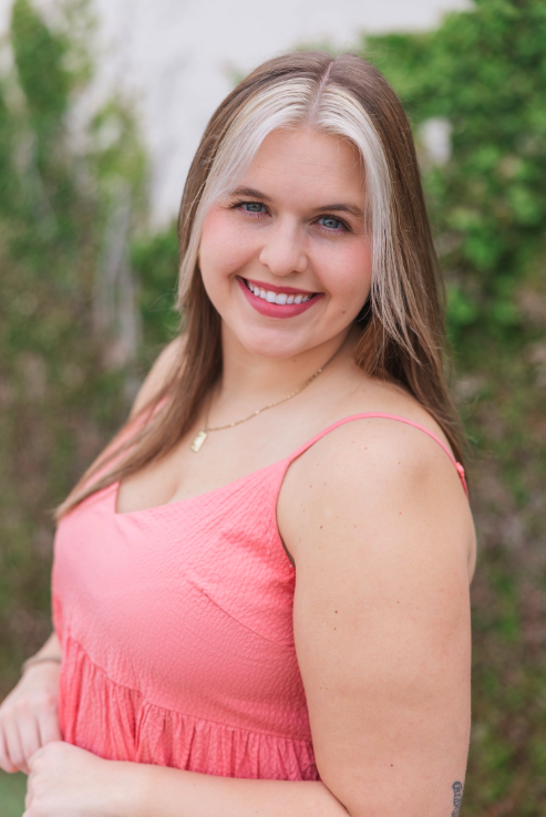 A young woman with blonde and brown hair in a pink dress on the Megan Mae Events team. 