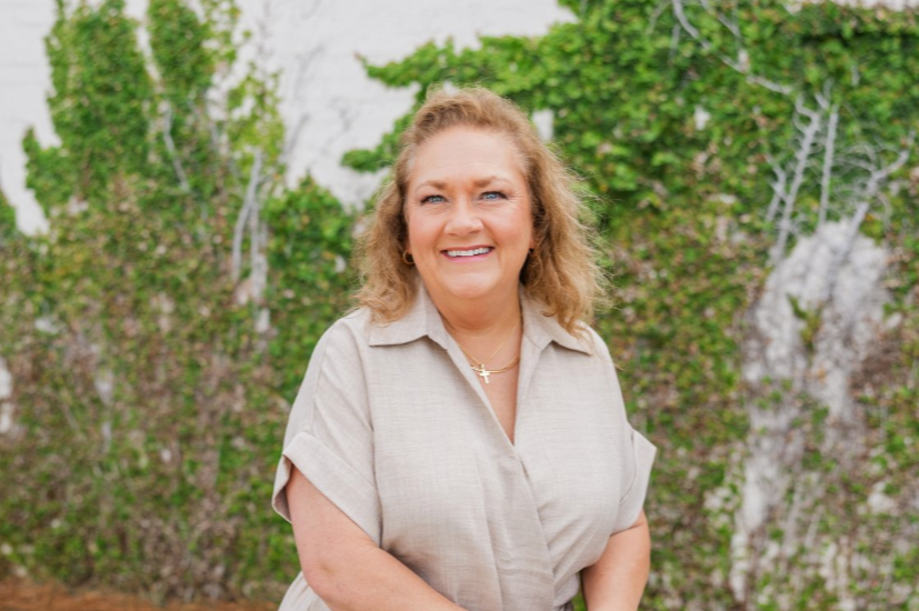 A joyful woman with curly brown hair in a tan dress on the Megan Mae Events team.