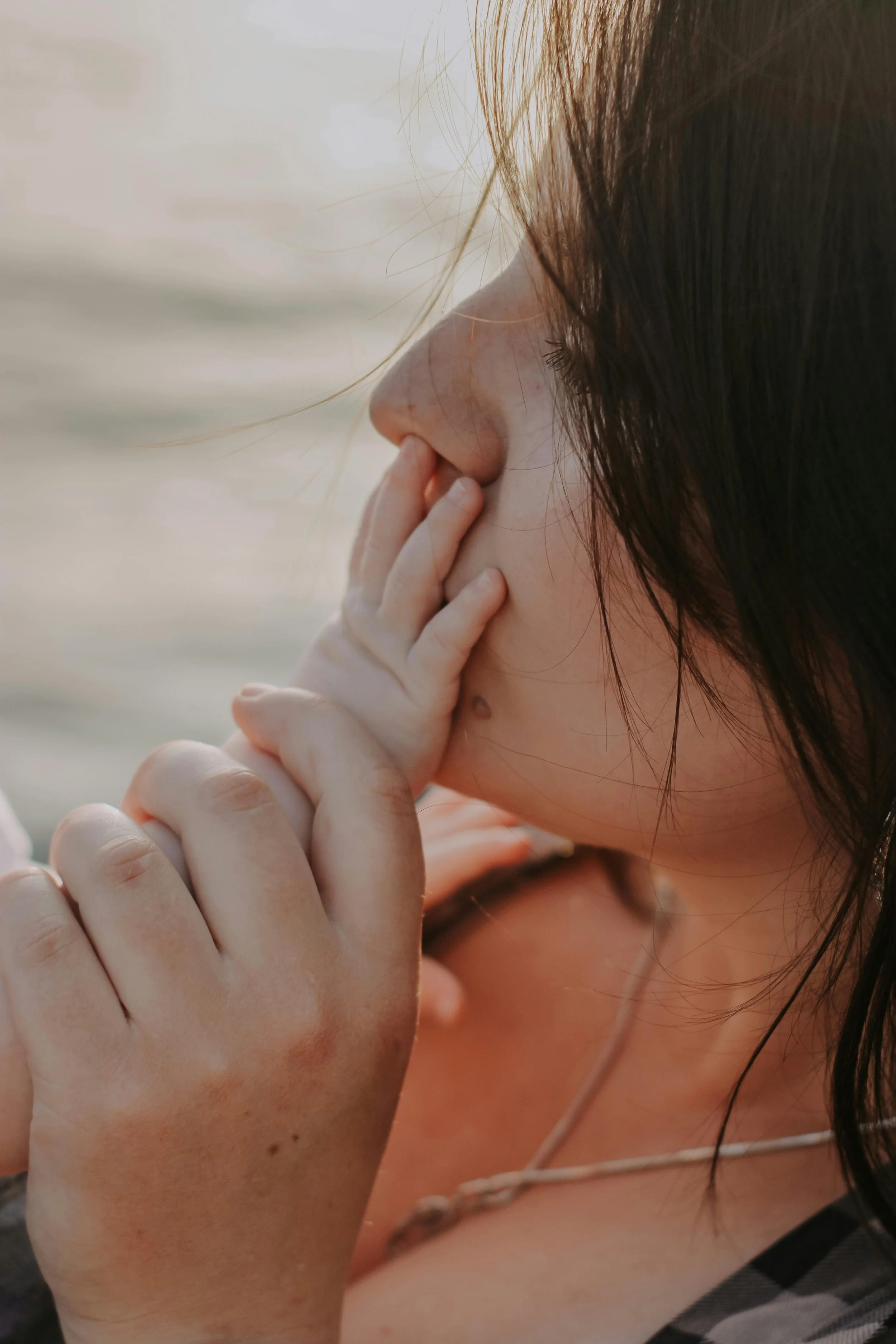 Close-up side profile of a woman with brown hair, holding her hand near her face, with a blurred background.