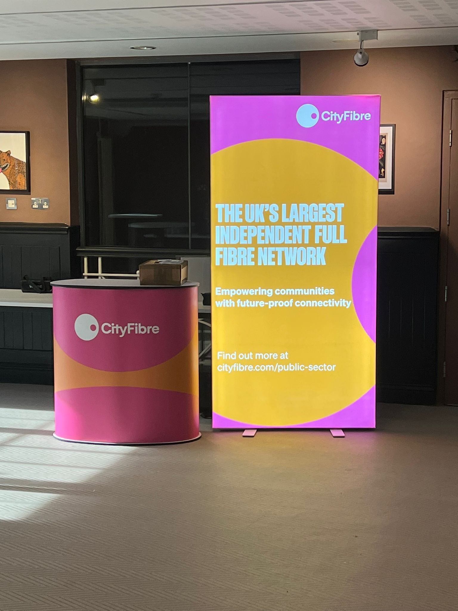 CityFibre promotional display with a pink and yellow banner stating 'The UK's Largest Independent Full Fibre Network' and a pink table with the CityFibre logo.