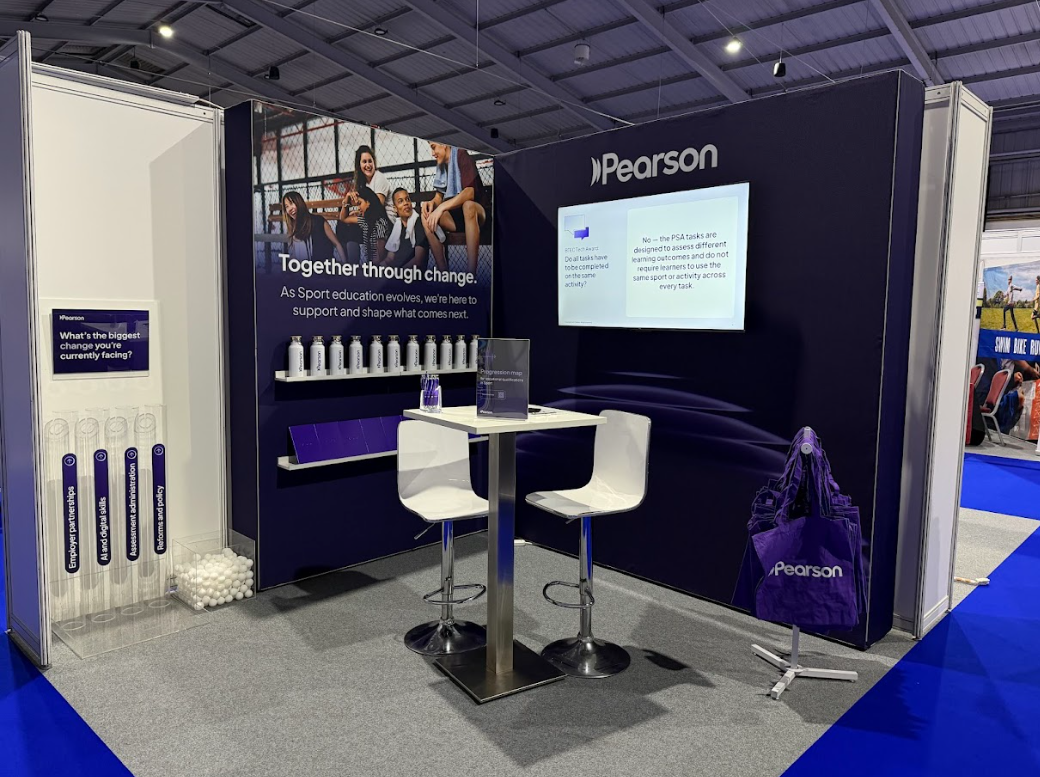 Pearson booth at a trade show with promotional materials, a screen displaying information, and seating area.