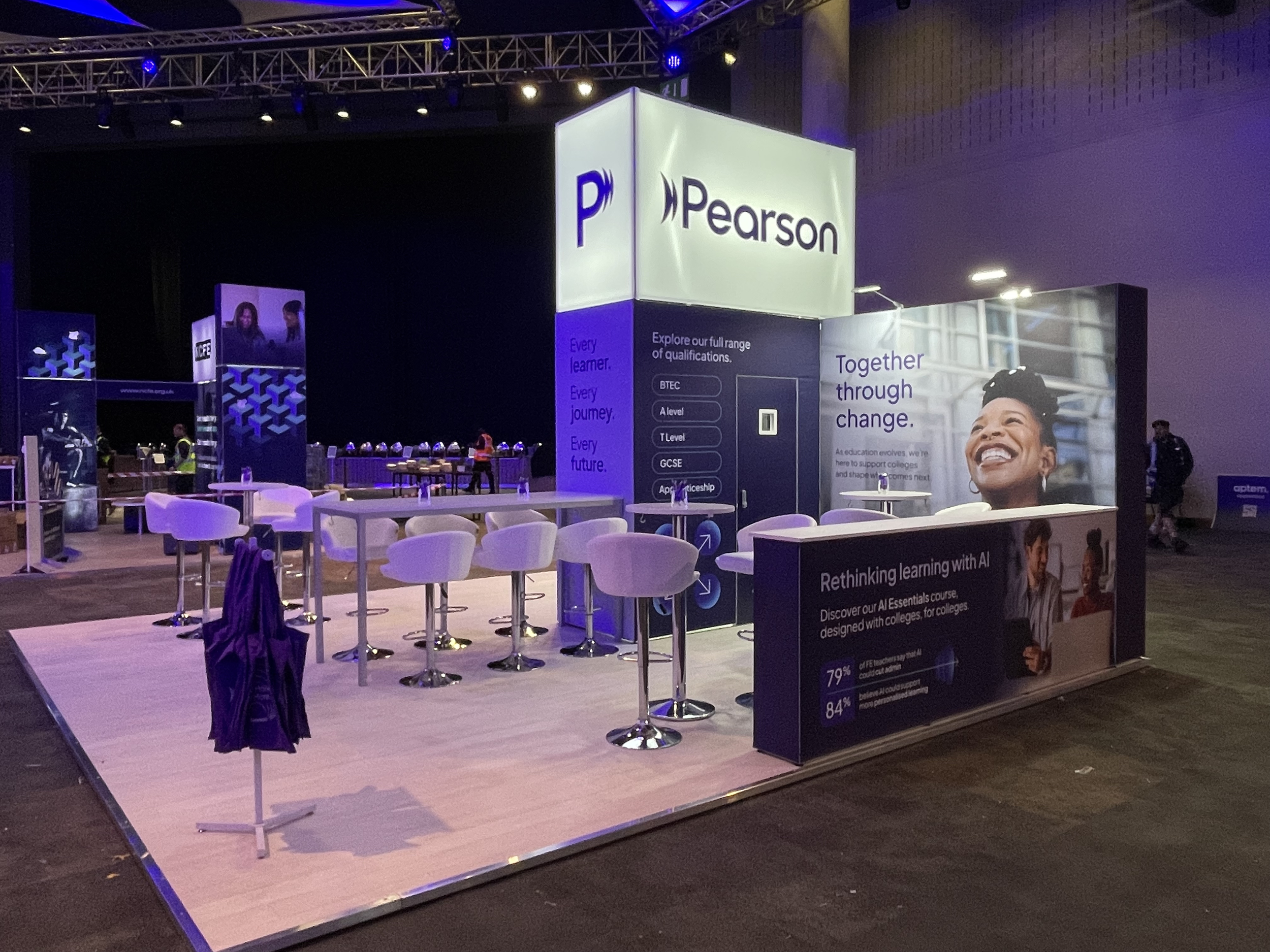 Exhibition booth for Pearson at a conference, featuring seating, informational posters, and branding displays with the slogan 'Together through change' and details about their AI learning courses.