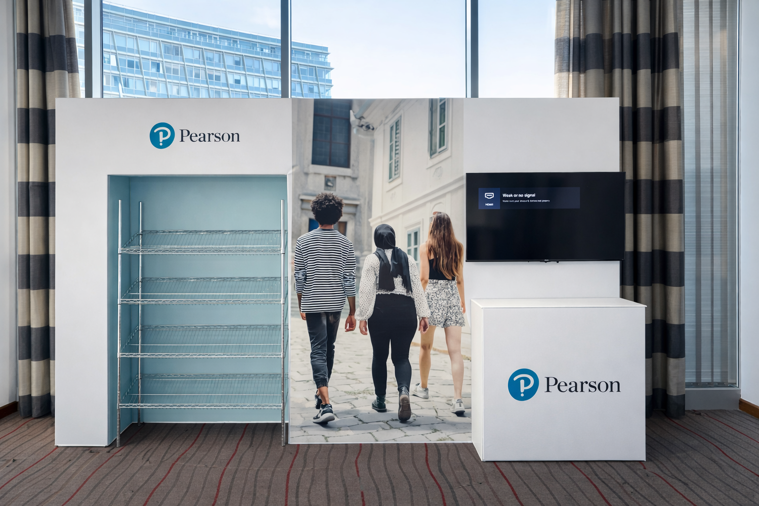 A Pearson display booth with an image of three young adults walking outdoors, a shelving unit on the left, a black screen on the right showing no signal, and a white counter with the Pearson logo in front of large window curtains.