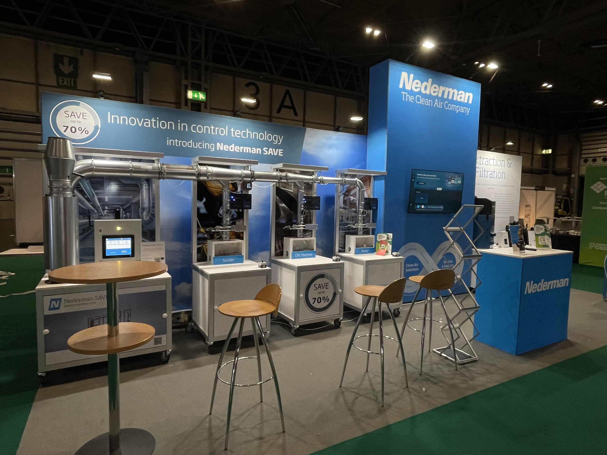Trade show booth for Nederman, featuring air control and filtration technology, with machinery, a digital display, and seating.