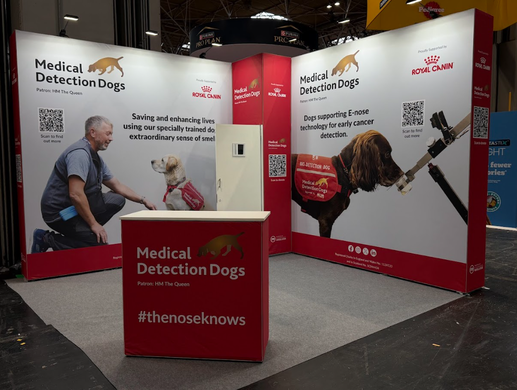 Booth display for Medical Detection Dogs and Royal Canin, featuring images of dogs and text about using trained dogs for medical detection, including cancer detection and early diagnosis.