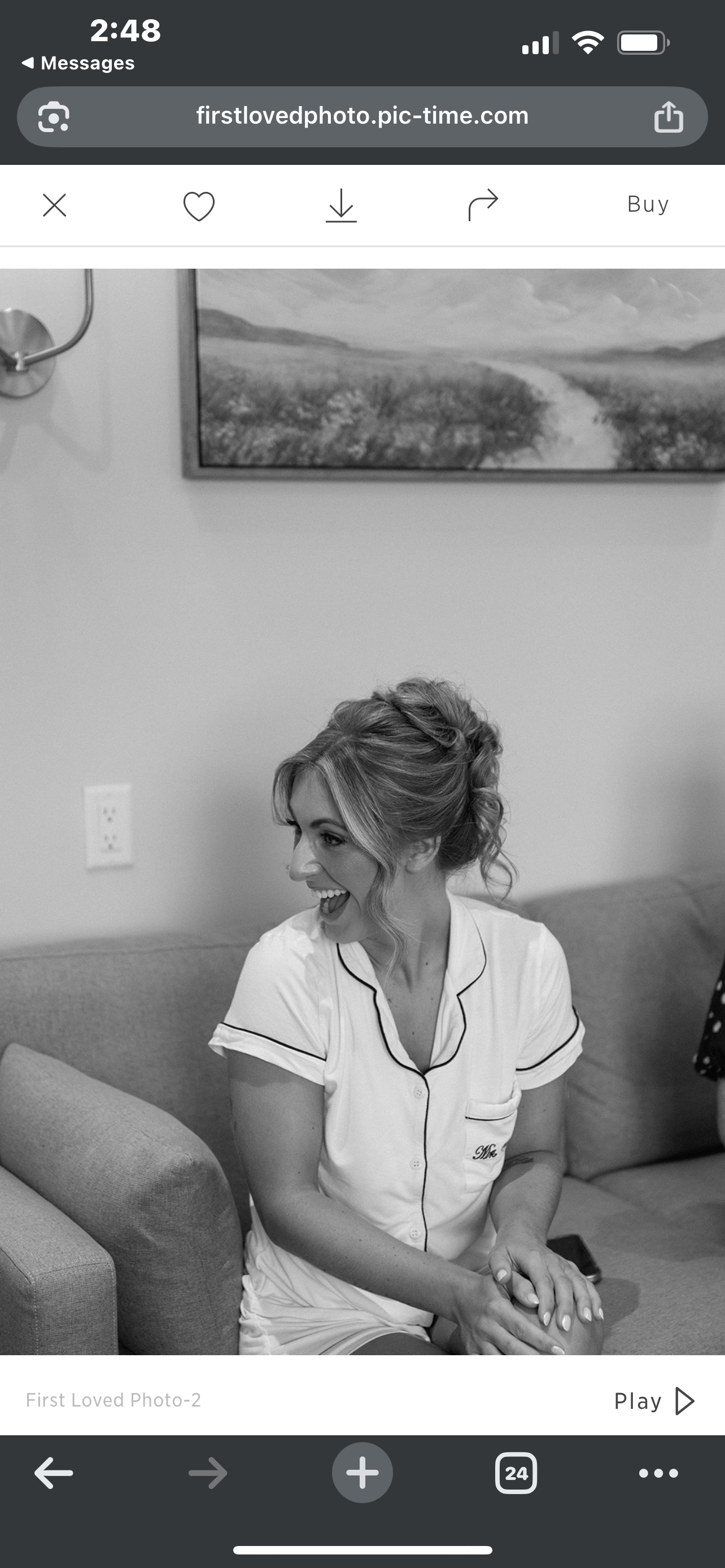 A woman with styled hair, smiling, sitting on a couch in a room with a landscape painting on the wall.