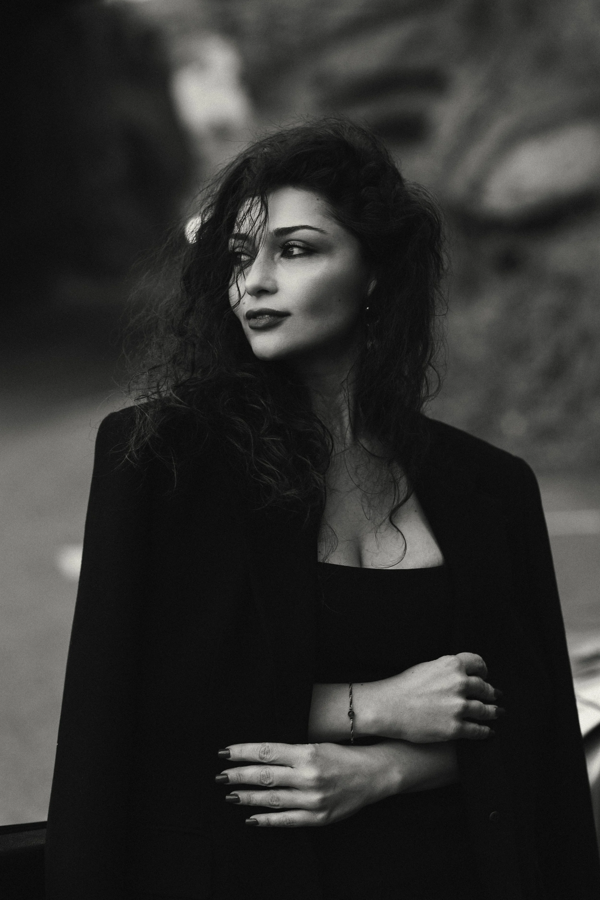 Black and white portrait of a woman with curly hair wearing a dark outfit and standing outdoors.