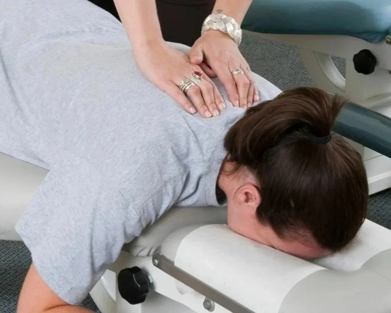 Person receiving chiropractic treatment while lying face down on a padded table, with hands of a practitioner using a massage technique on their back.