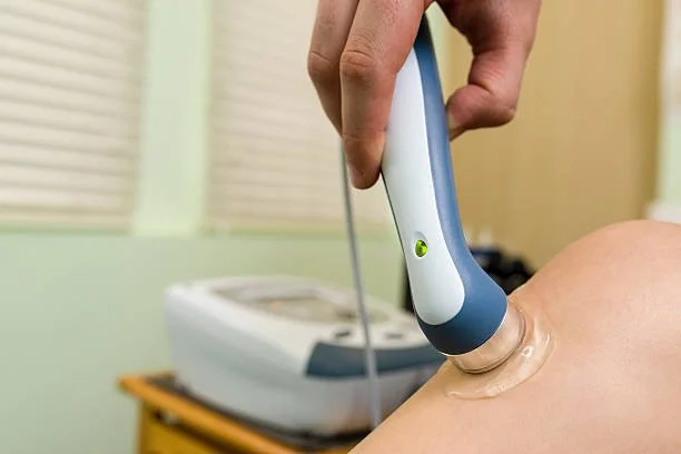 Person using an ultrasound device on a patient's knee in a medical setting.