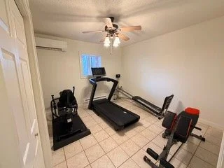 Home gym with treadmill, rowing machine, and exercise bike, in a small room with white walls, tiled floor, ceiling fan, and a small window.