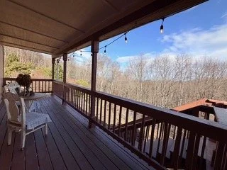 View from a covered wooden porch overlooking trees and a partly cloudy sky.
