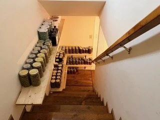 Several jars and bottles of various sizes on white wooden shelves along a staircase wall.