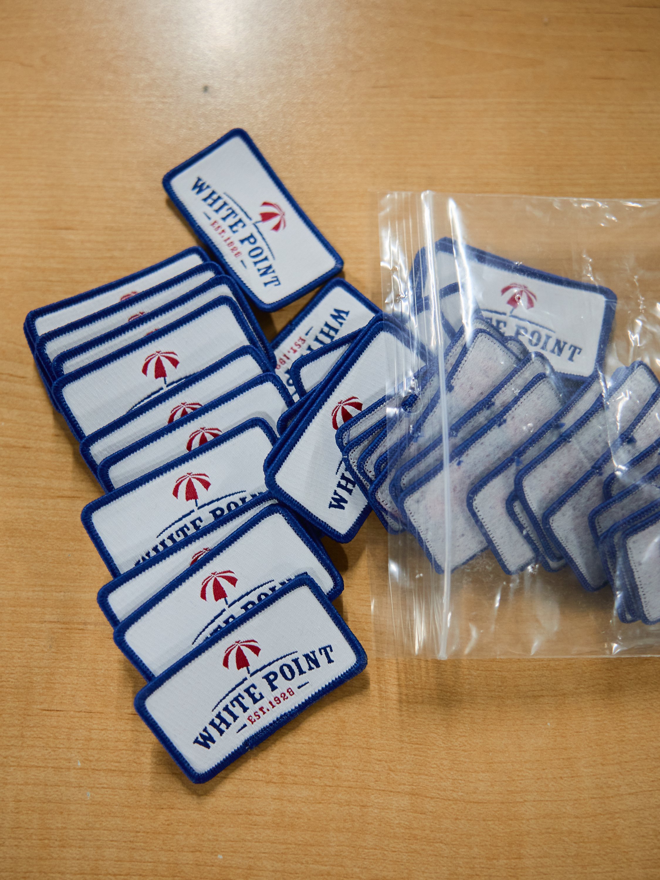 A collection of White Point embroidered patches, some in a plastic bag, on a wooden surface.