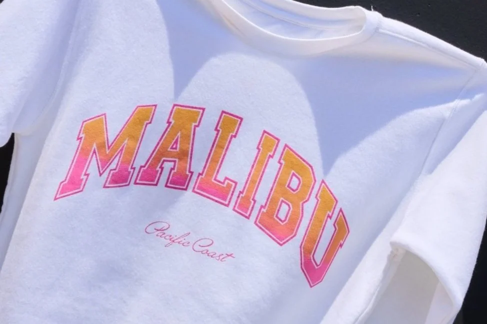 White T-shirt with the word MALIBU in large, colorful, gradient letters and PACIFIC COAST written below in smaller, cursive font.