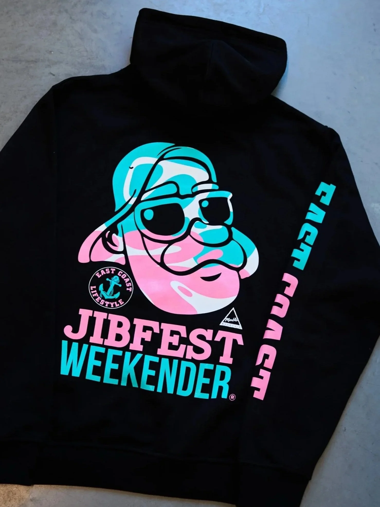 Black hoodie with a colorful graphic of a bearded man wearing sunglasses and a cap, with the text "JIBFEST" in pink and "WEEKENDER" in blue, along with smaller logos that say "EAST COAST LIFESTYLE."