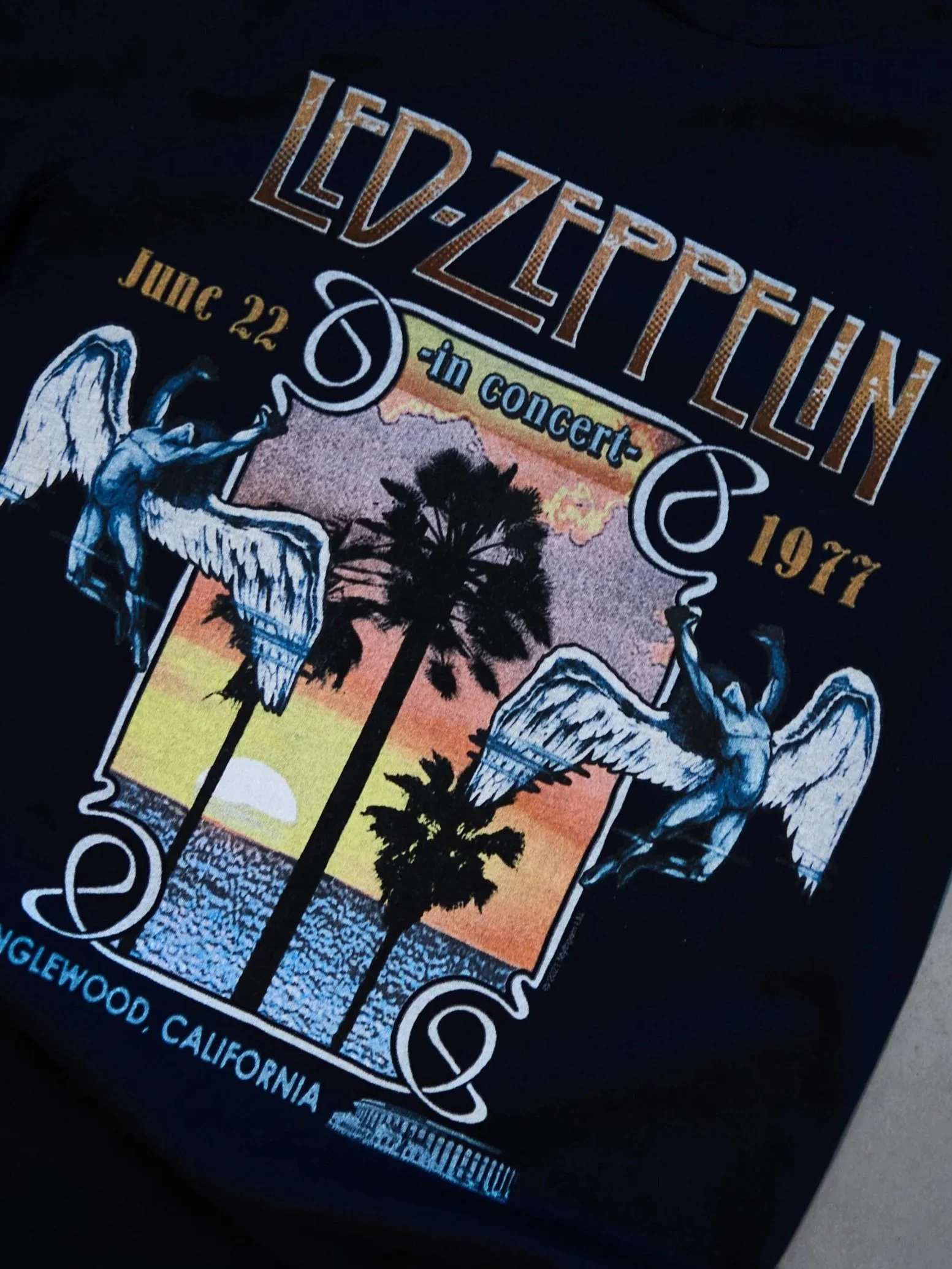 Black Led Zeppelin concert T-shirt featuring a Sunset with palm trees, angels, and decorative elements, with text indicating the concert date of June 22, 1977, in Inglewood, California.