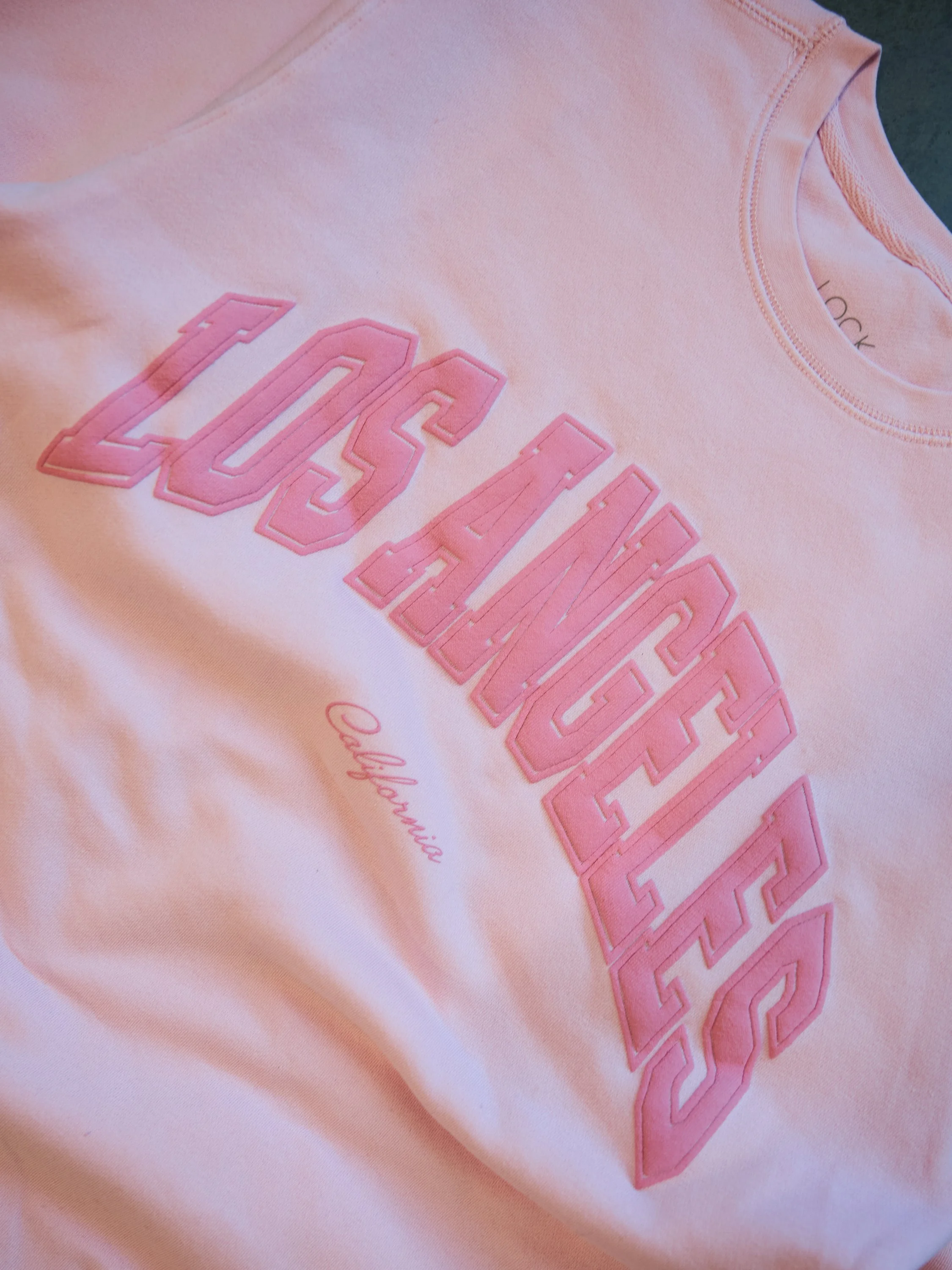 Pink California Dreaming t-shirt with large embroidered text and smaller cursive text."California"