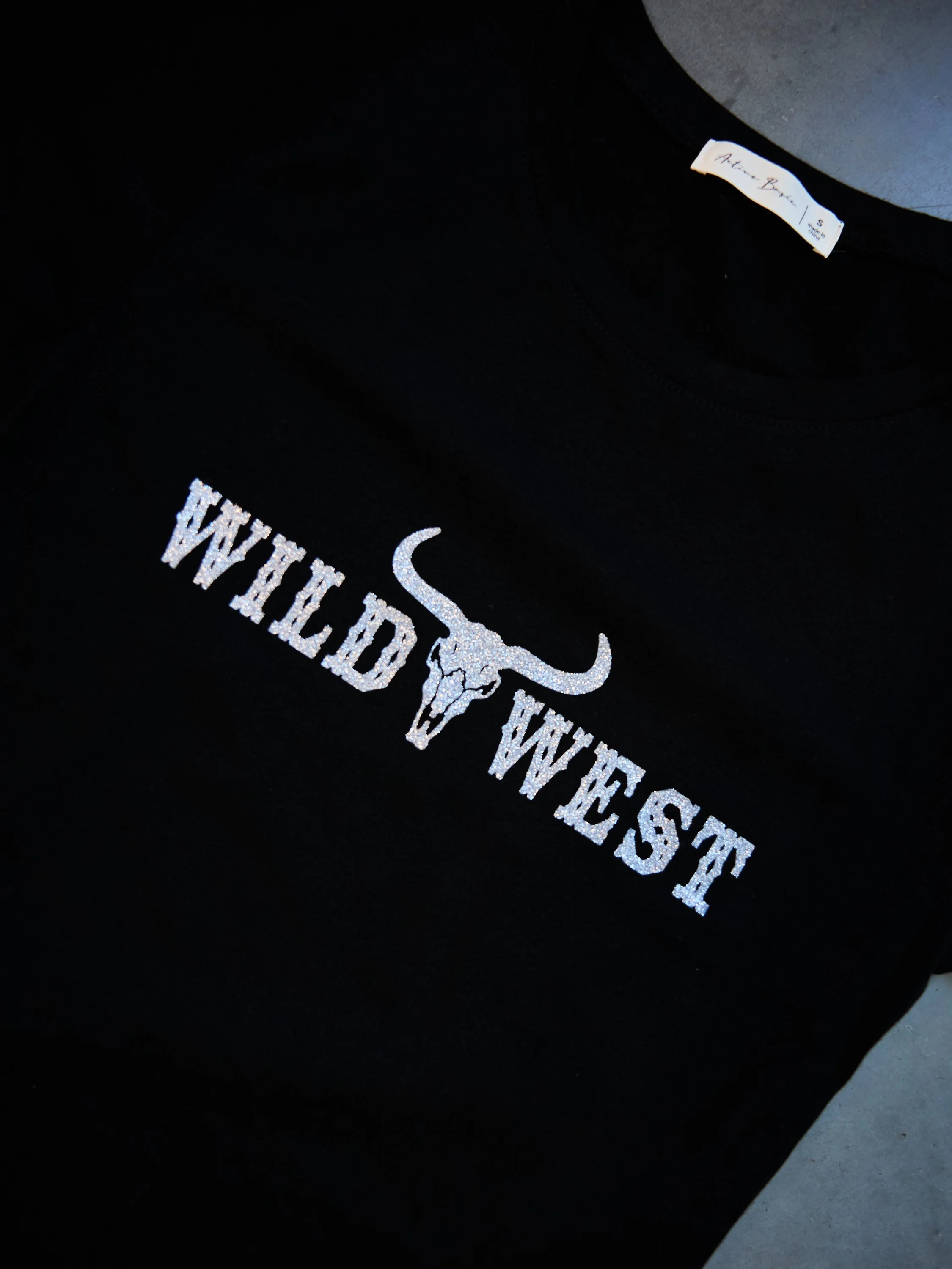 Black t-shirt with white glittery text and a longhorn skull graphic reading "WILDCAT WRESTLING." The shirt also has a tag that reads "A-Town Boon 1 S."