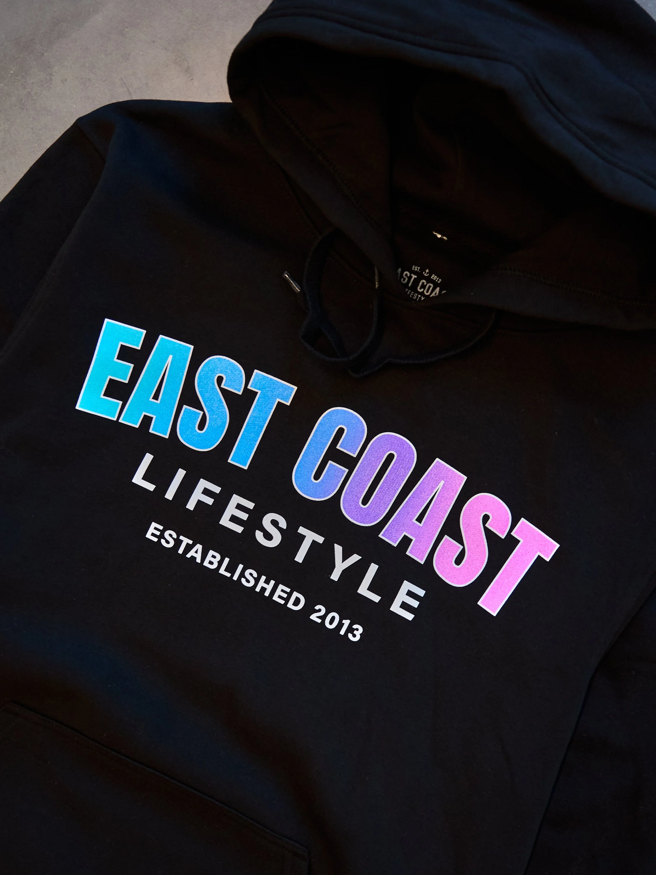 Close-up of a black hoodie with colorful text that reads 'EAST COAST LIFESTYLE ESTABLISHED 2013'.