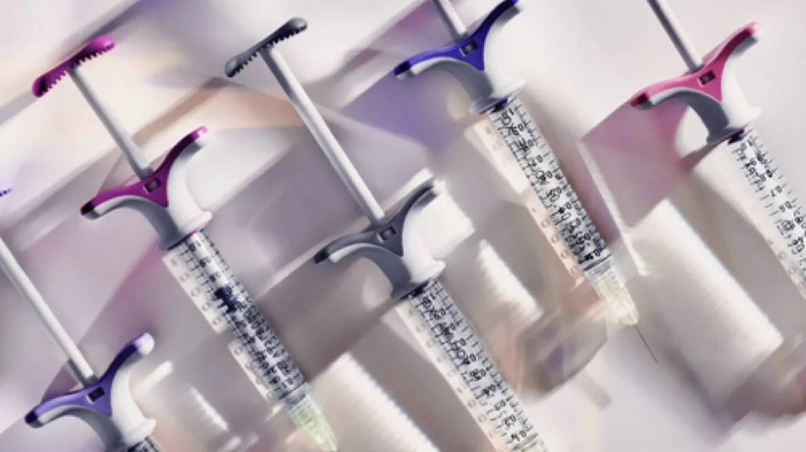 Multiple syringes filled with a clear liquid, arranged diagonally on a surface.
