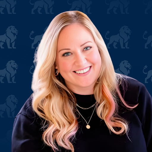 A young woman with long blonde hair and pink tips, smiling with teeth, wearing gold hoop earrings, a black top, and layered gold necklaces, against a blue backdrop with a lion logo pattern.