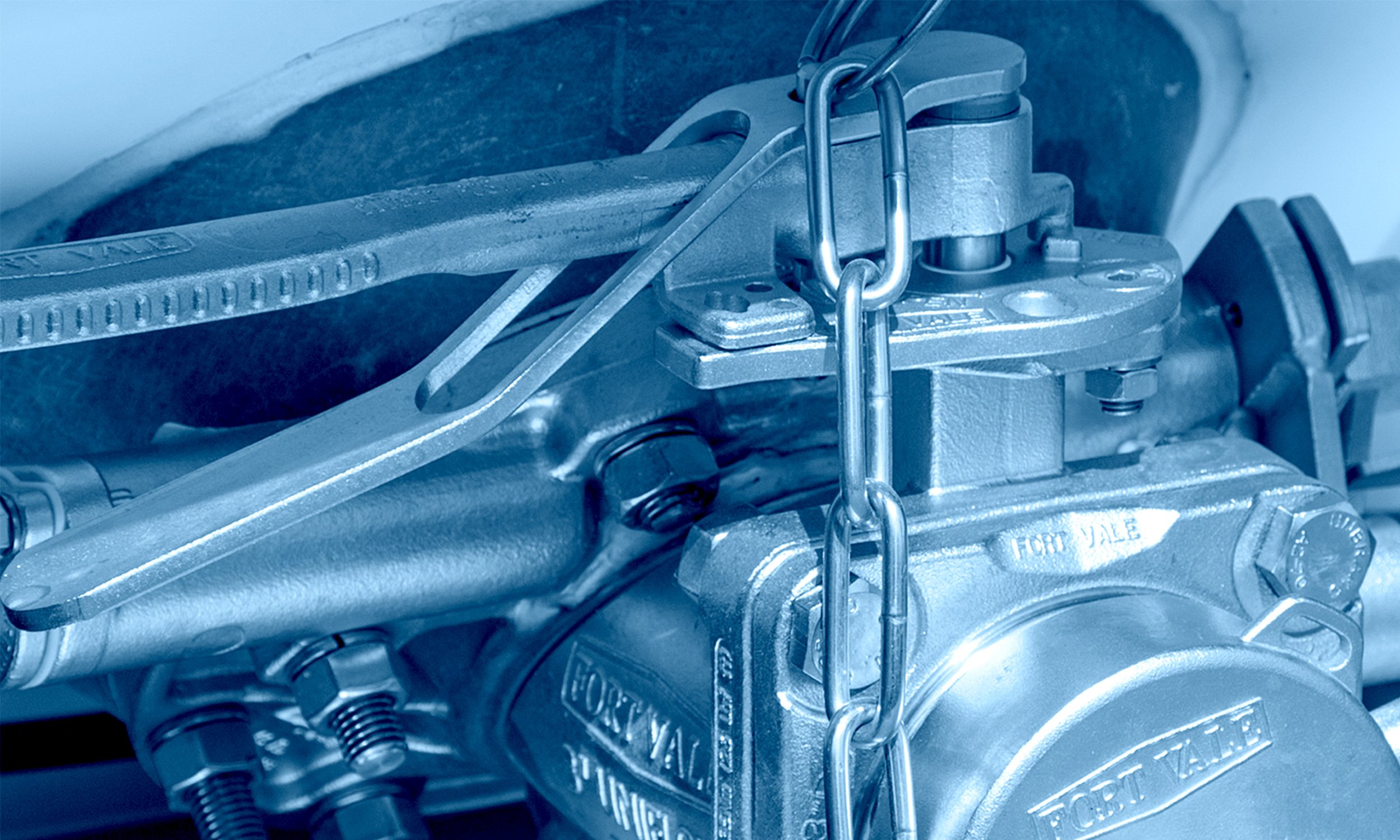 A close-up view of an engine block with a chain attached, part of a mechanical assembly, showing various metallic components including bolts, a gear, and a chain guide.