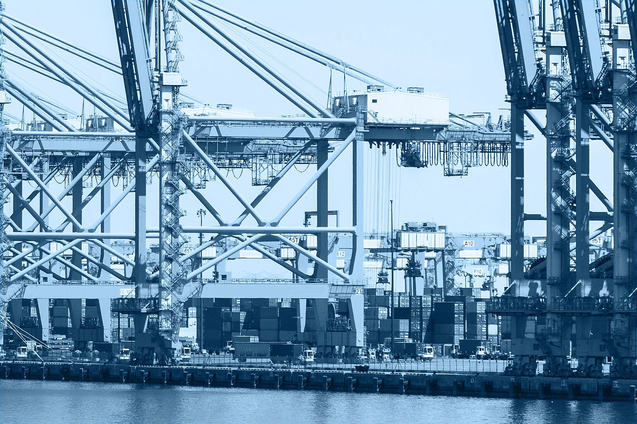 Industrial port with large cranes and shipping containers, near water, under clear sky.
