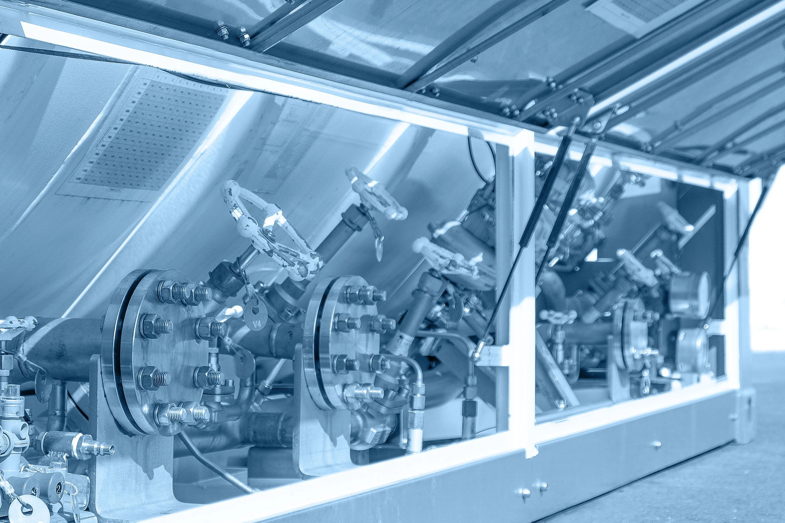 Close-up of a metallic industrial machine with various pipes, valves, and hardware components, illuminated by bright fluorescent lighting.