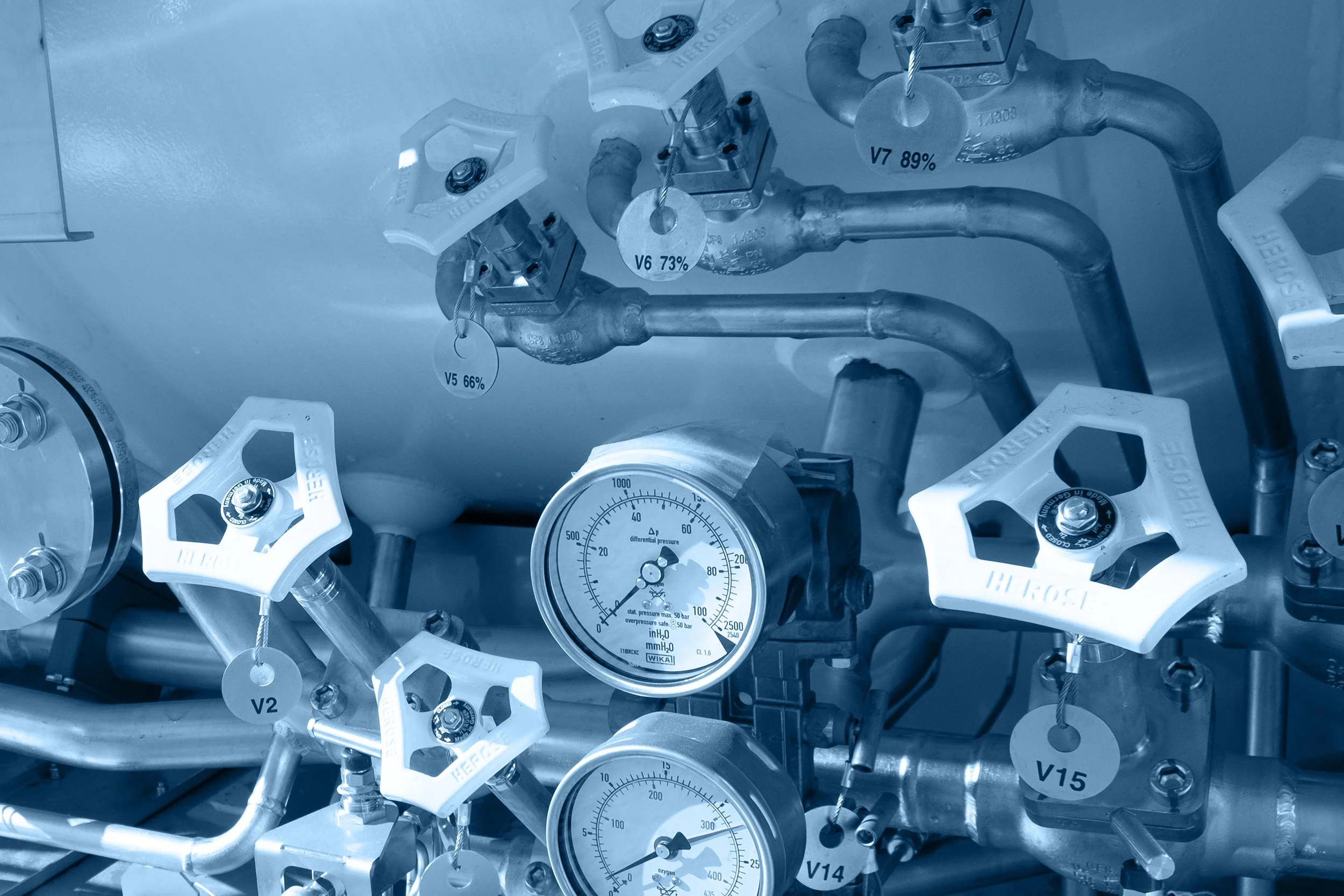 Close-up of industrial pressure gauges and valves with labels and tags attached, part of a larger machinery system.