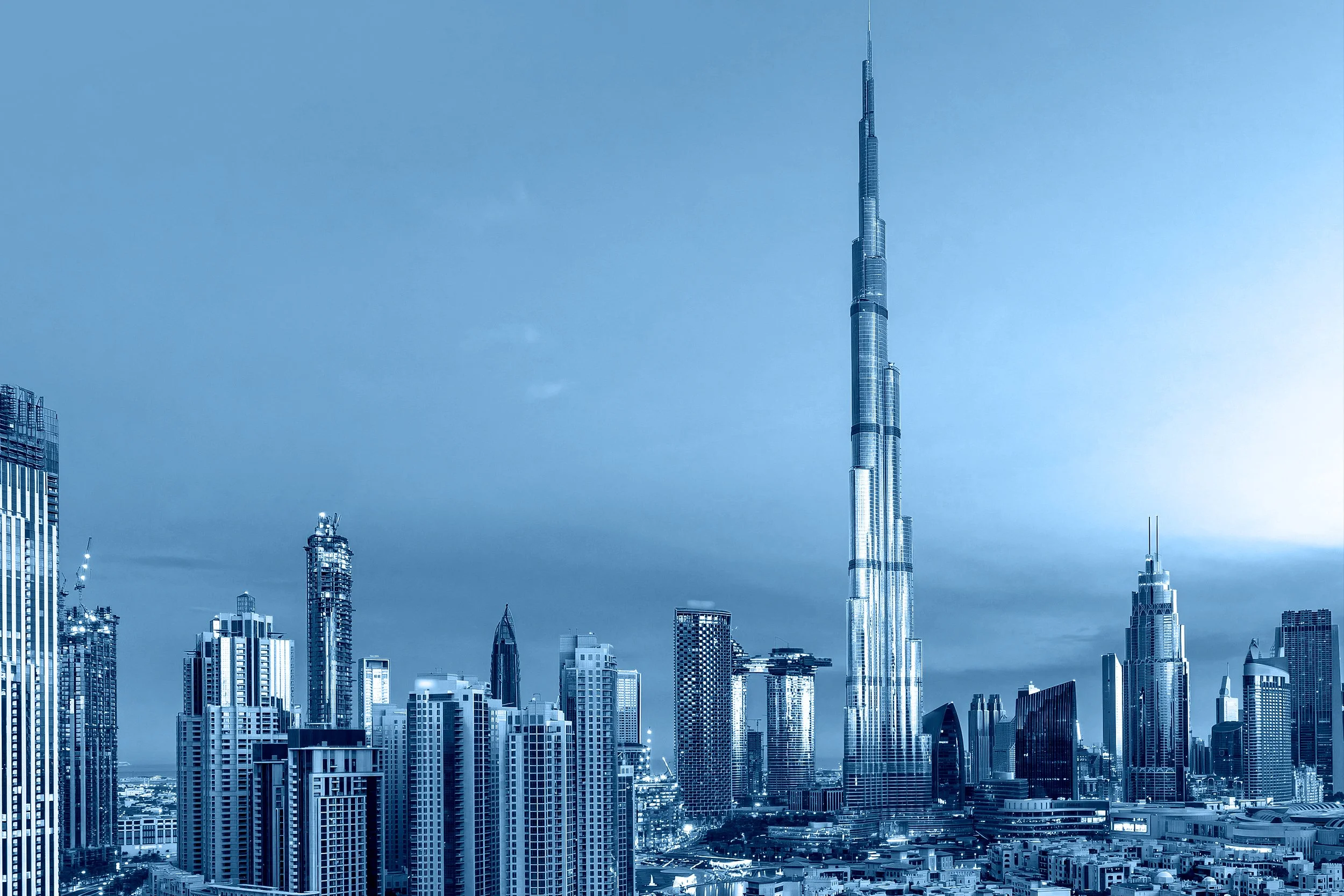 Skyline of Dubai with tall skyscrapers, including the Burj Khalifa, during nighttime with city lights.