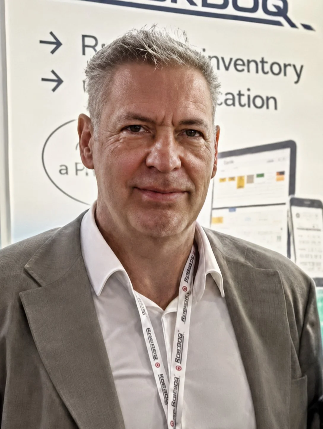 A man in a light gray suit and white shirt standing in front of a booth with a sign and digital display, wearing a lanyard with the Target logo from Robexec.
