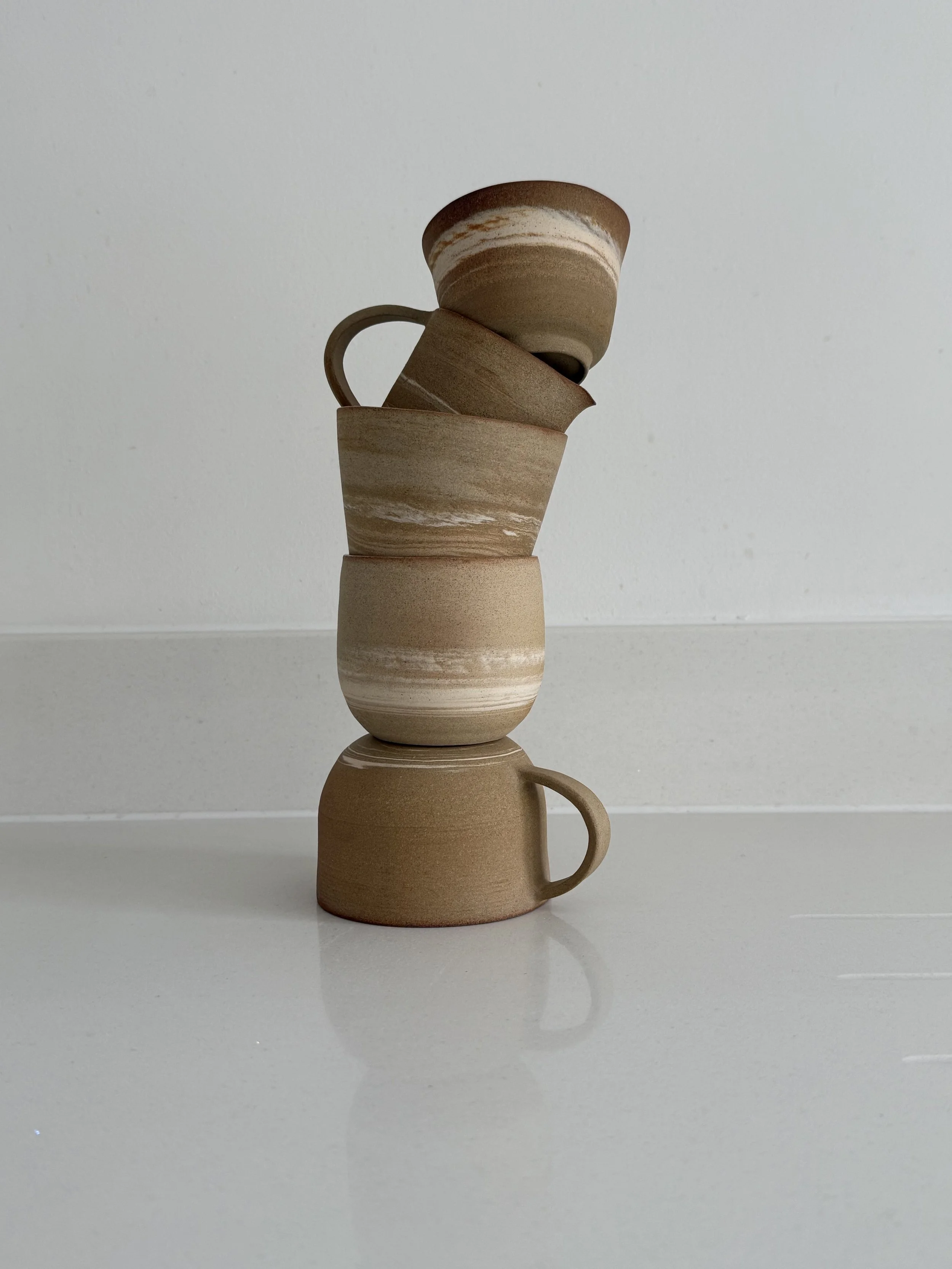 Stacked beige ceramic cups and mugs on a white surface with a white background.