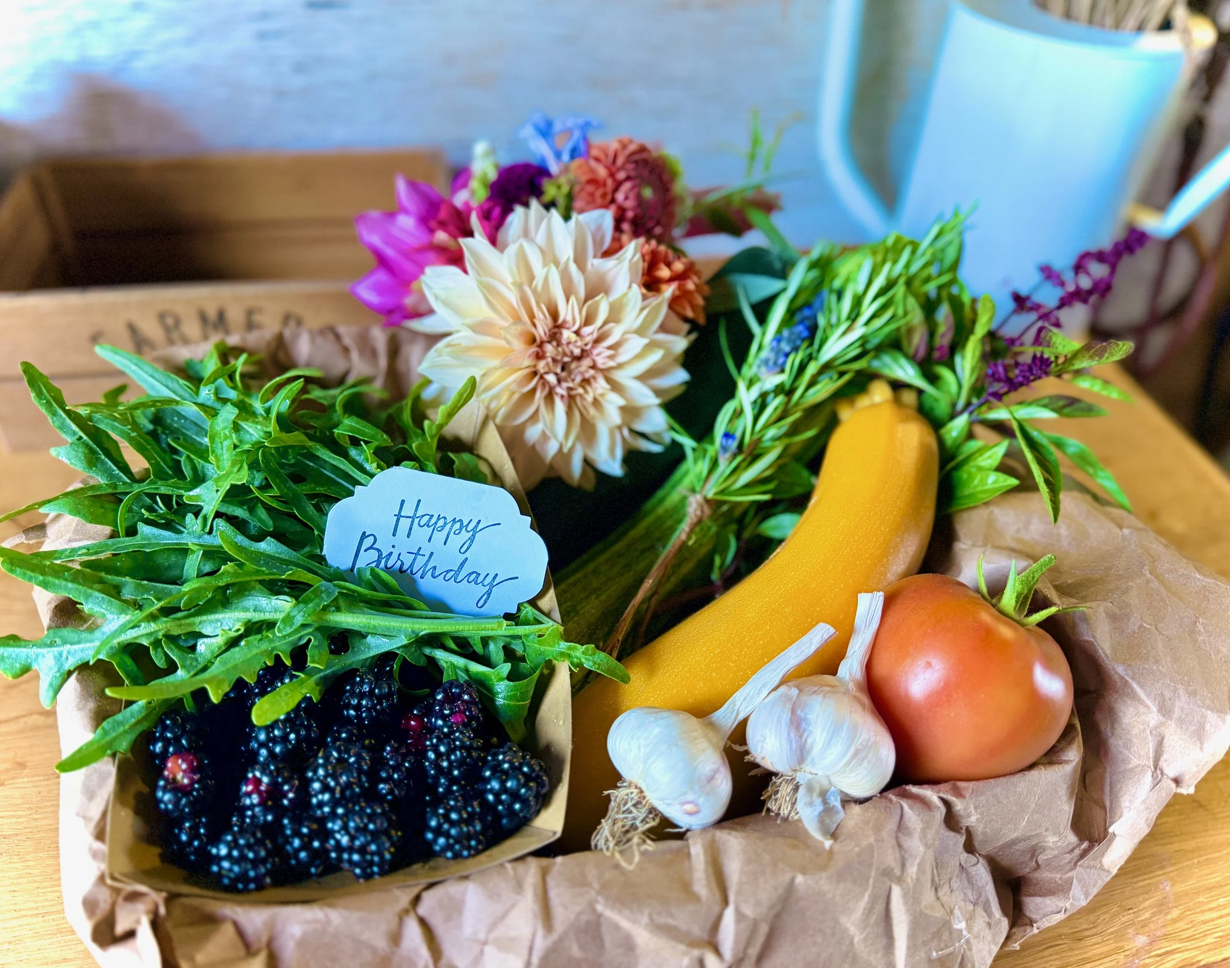 A gift basket with assorted vegetables, berries, flowers, and a small note that says 'Happy Birthday' on a wooden surface.