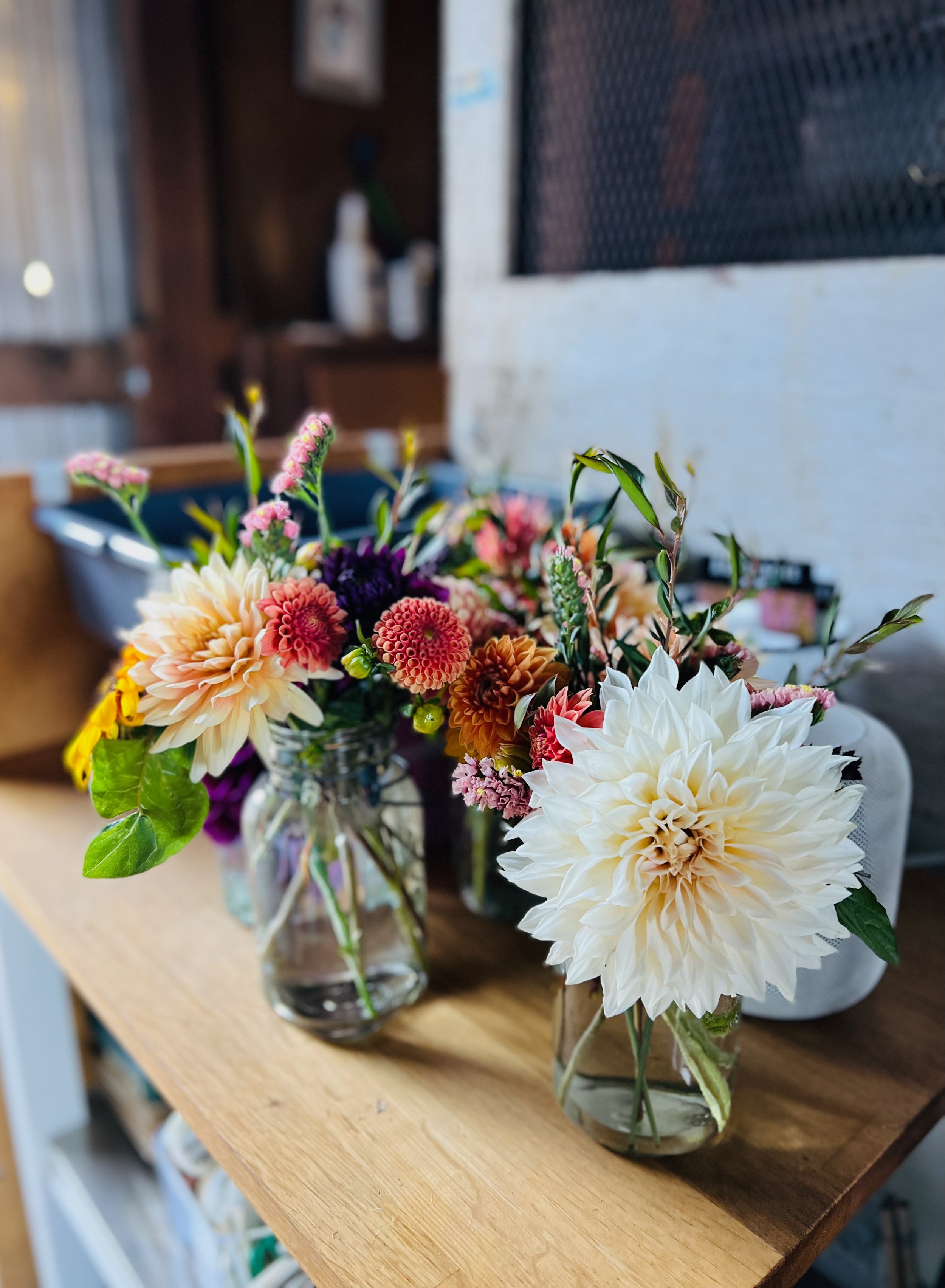 Two glass jars with colorful flowers on a wooden surface inside a cozy barn.
