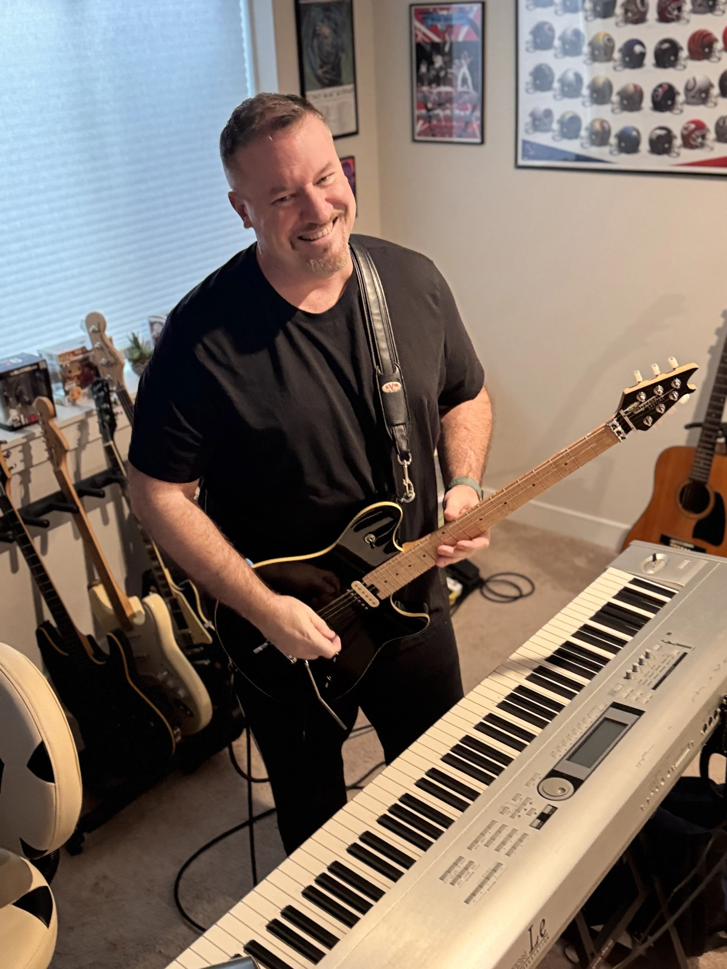 Jeff Warren holding a guitar and standing in front of a keyboard.