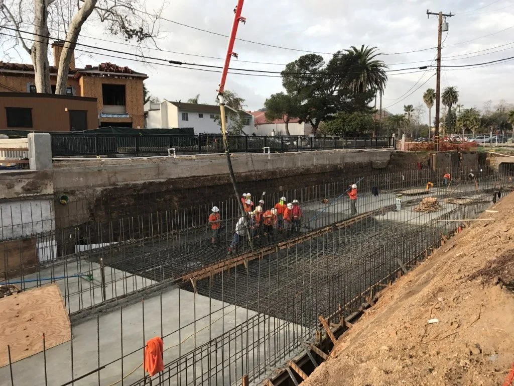 Construction workers wearing safety gear and helmets working on rebar framework for building foundation on a construction site.