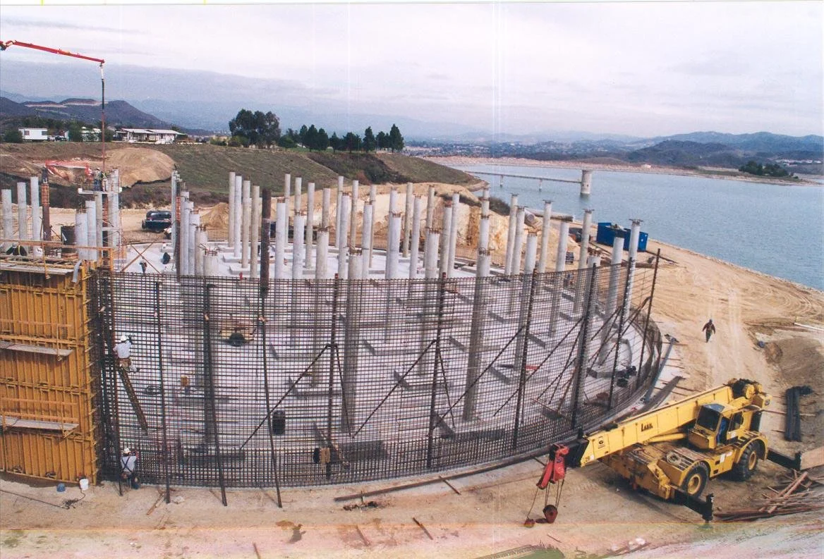 Construction site near a body of water with numerous vertical concrete columns and a yellow crane.