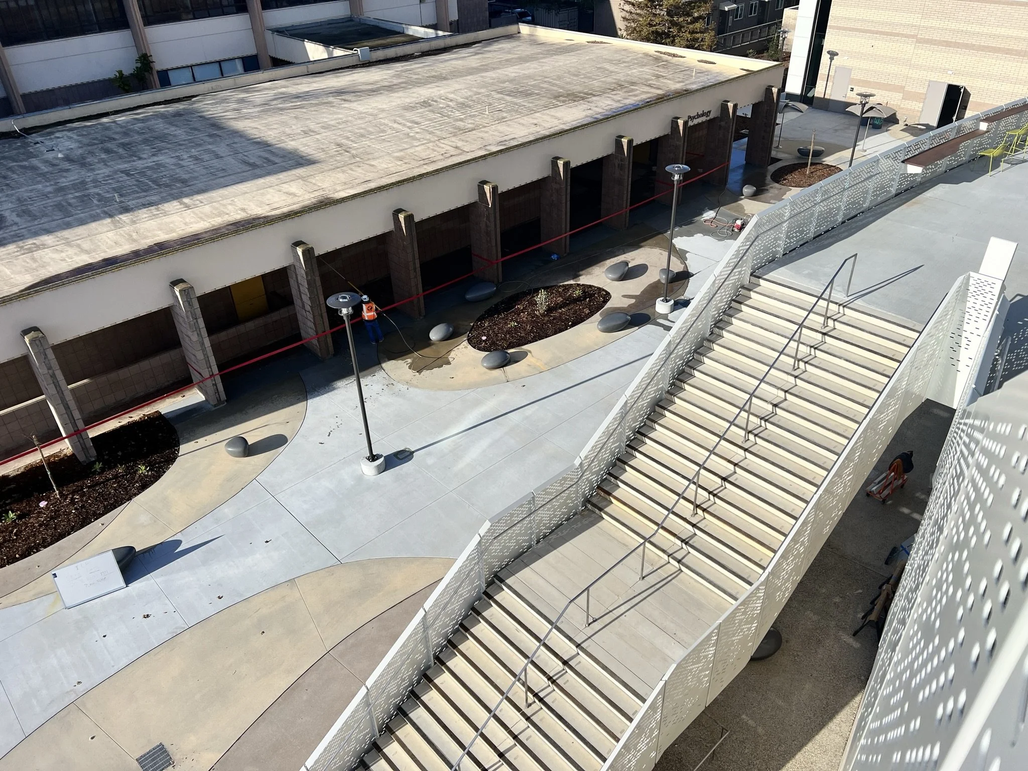 An outdoor area on a rooftop or balcony with stairs, modern black chairs, and textured white fencing.