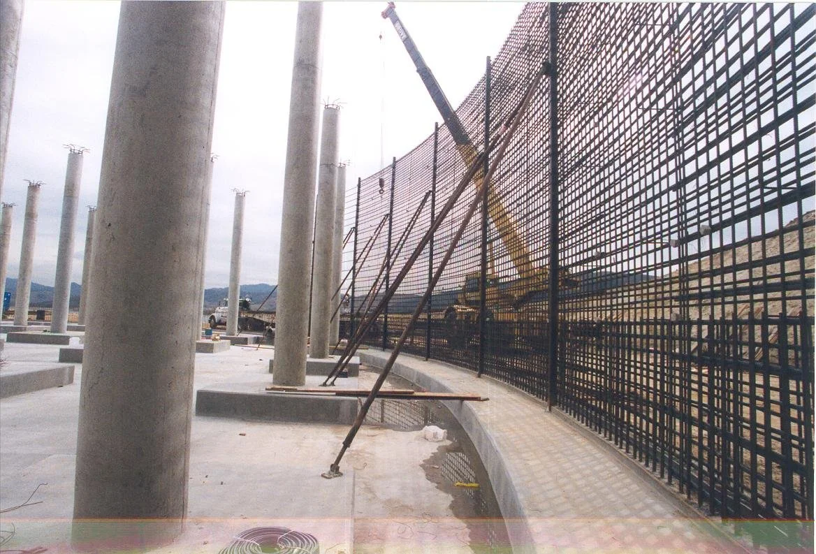 Construction site with large concrete pillars, a crane, and a steel fence.