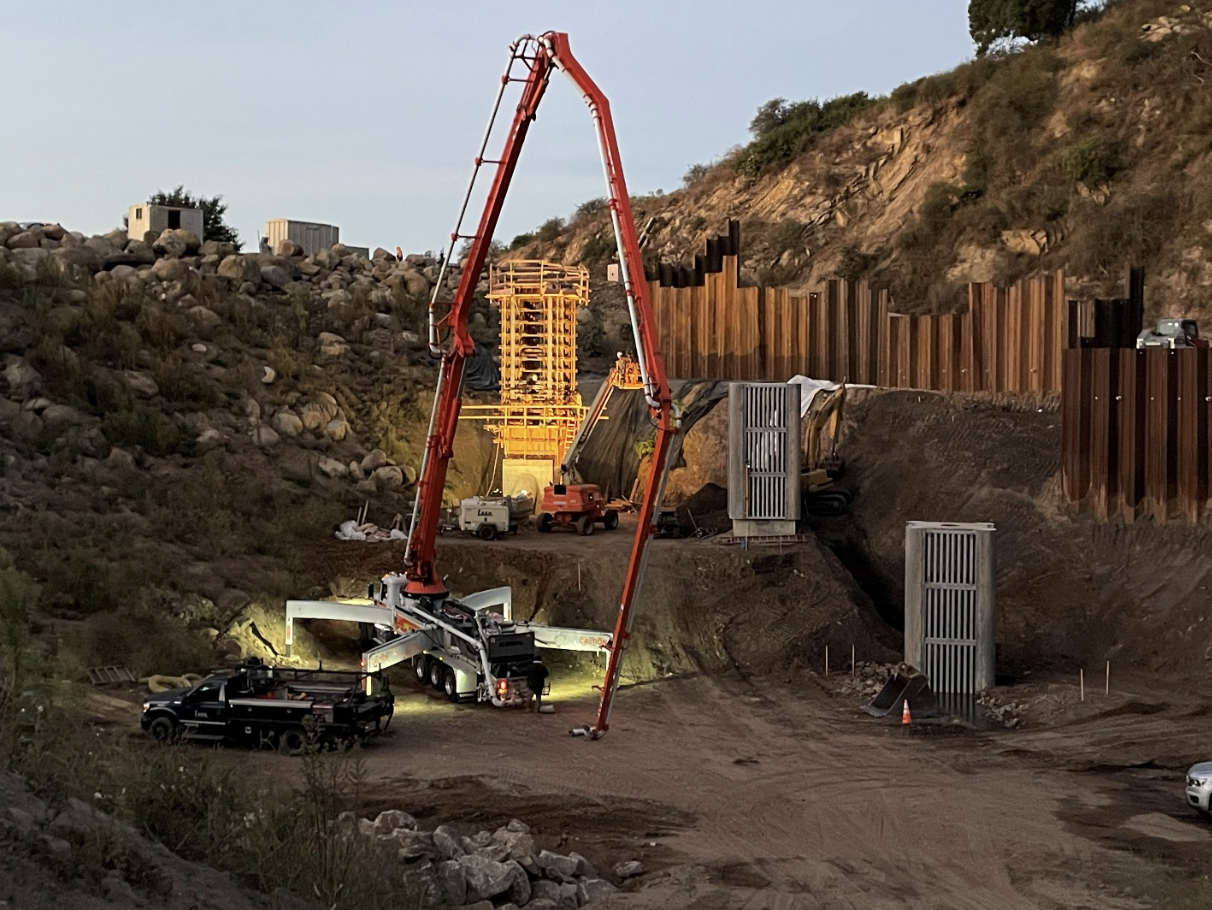 Construction site on a hillside with cranes, heavy machinery, and safety barriers installing a large metal structure.