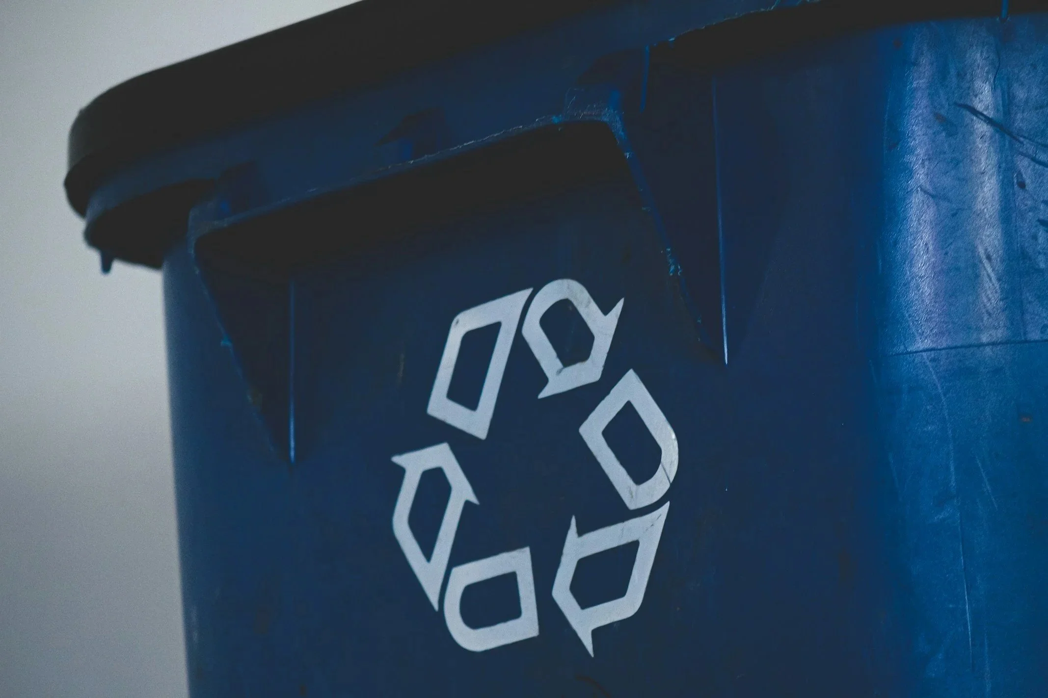 Close-up of a blue recycling bin with a white recycling symbol.