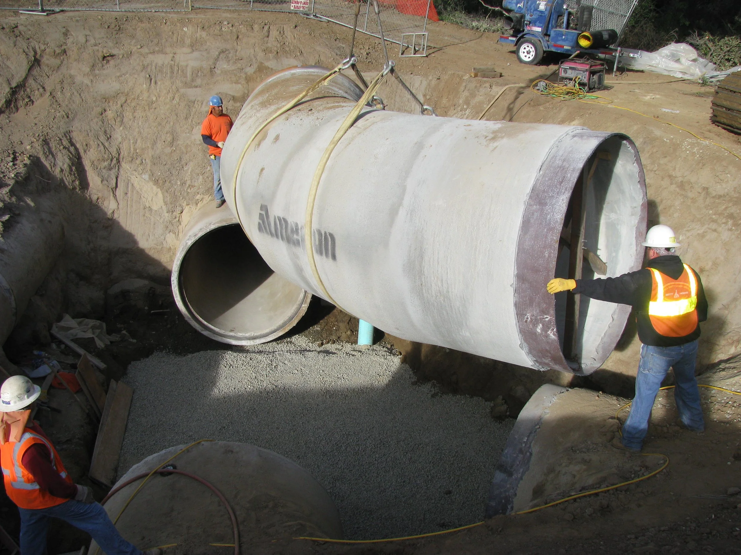 Construction workers placing large concrete pipes in a trench at a construction site.