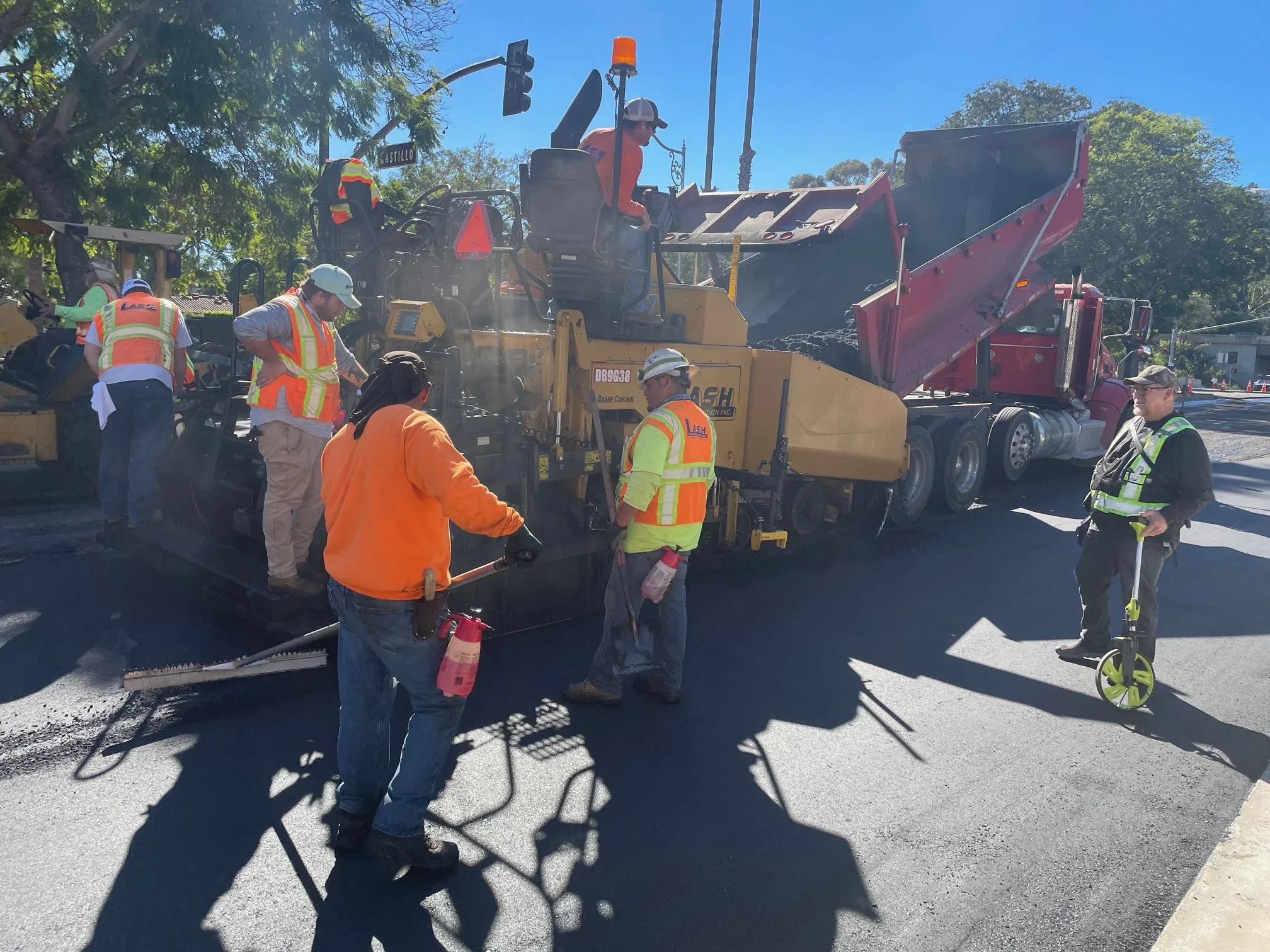 Construction workers paving a road with asphalt using a paving machine on a sunny day.