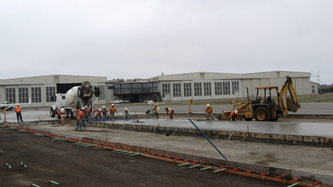 Construction workers pouring and smoothing concrete for a new road at an airport.