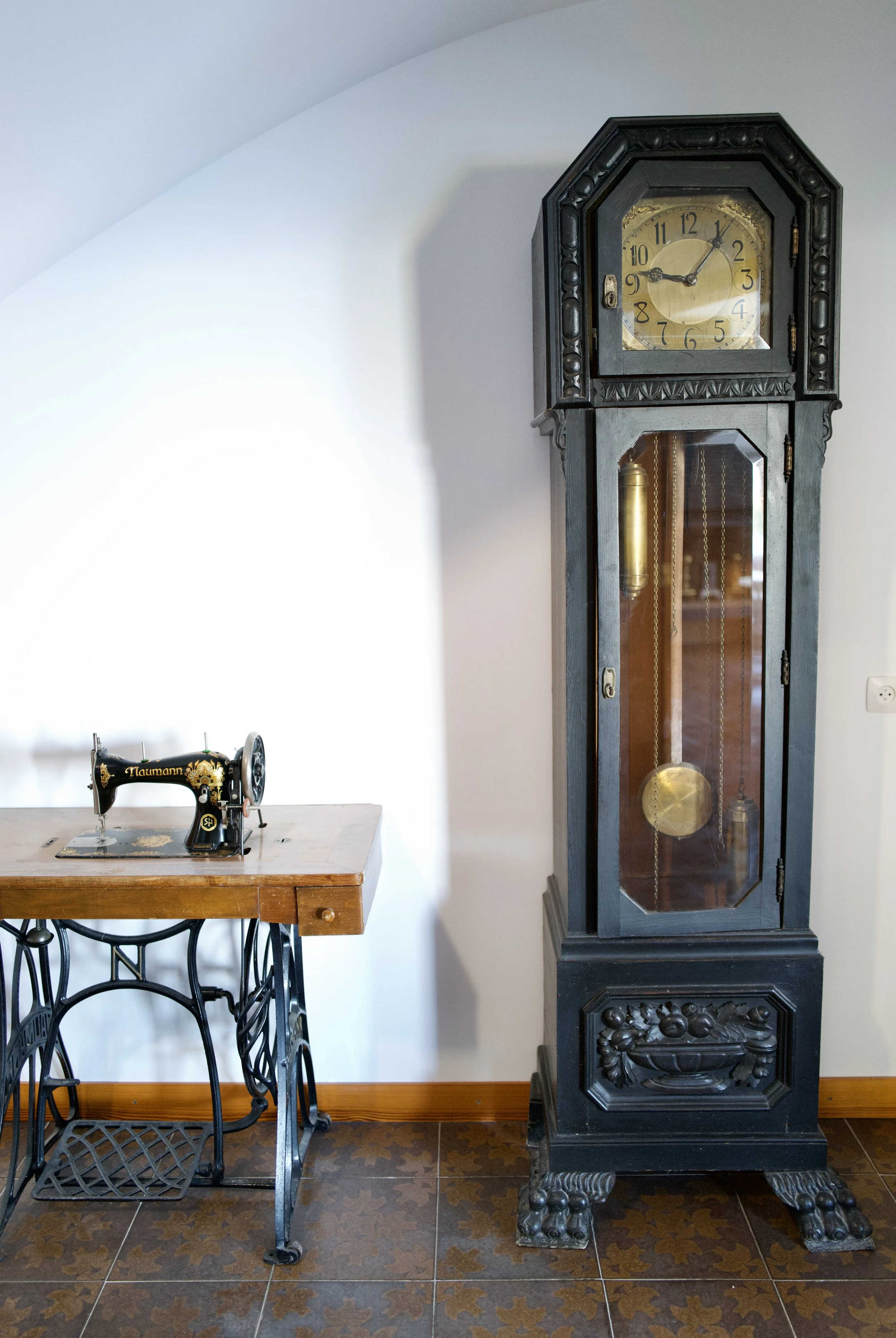 Reloj de caja alta y maquina de coser antigua de la prestigiosa marca Nauman en el recibidor amplio y luminoso en la casa de alquiler Ca la Nuri en la playa del Lané en Cadaqués.