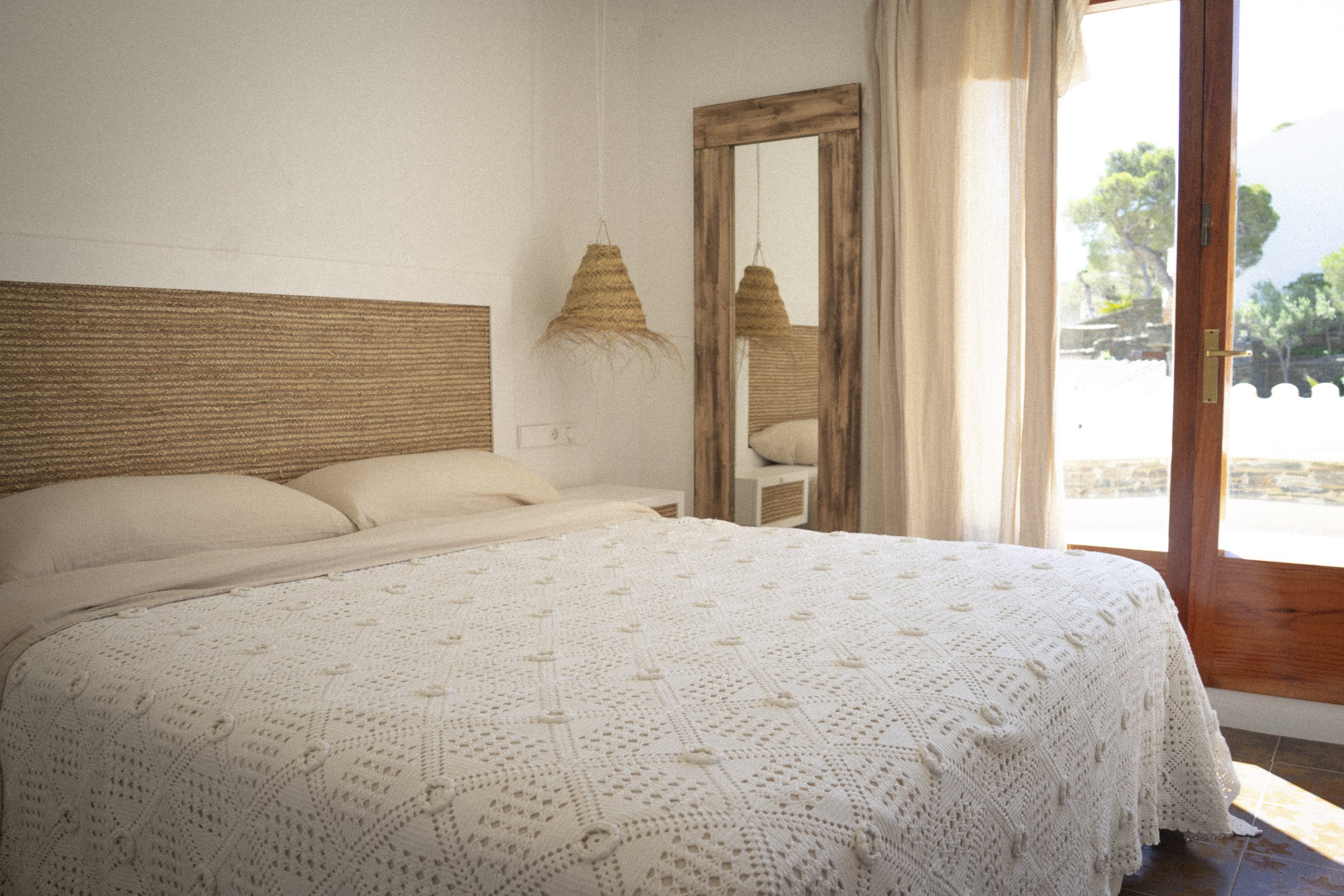 Habitación doble exclusiva en la casa de alquiler a primera linea de mar. Ca la Nuri Cadaqués. Dispone de una terraza con vistas a la montaña y al mar. Decorada con cubrecama artesanal de ganchillo y lámparas de esparto. 