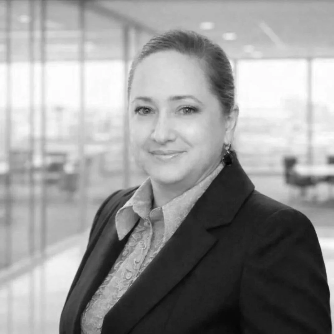 A black and white portrait of a woman in a business suit with an office background.