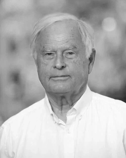 Black and white portrait of an elderly man with white hair, wearing a collared shirt, looking directly at the camera.