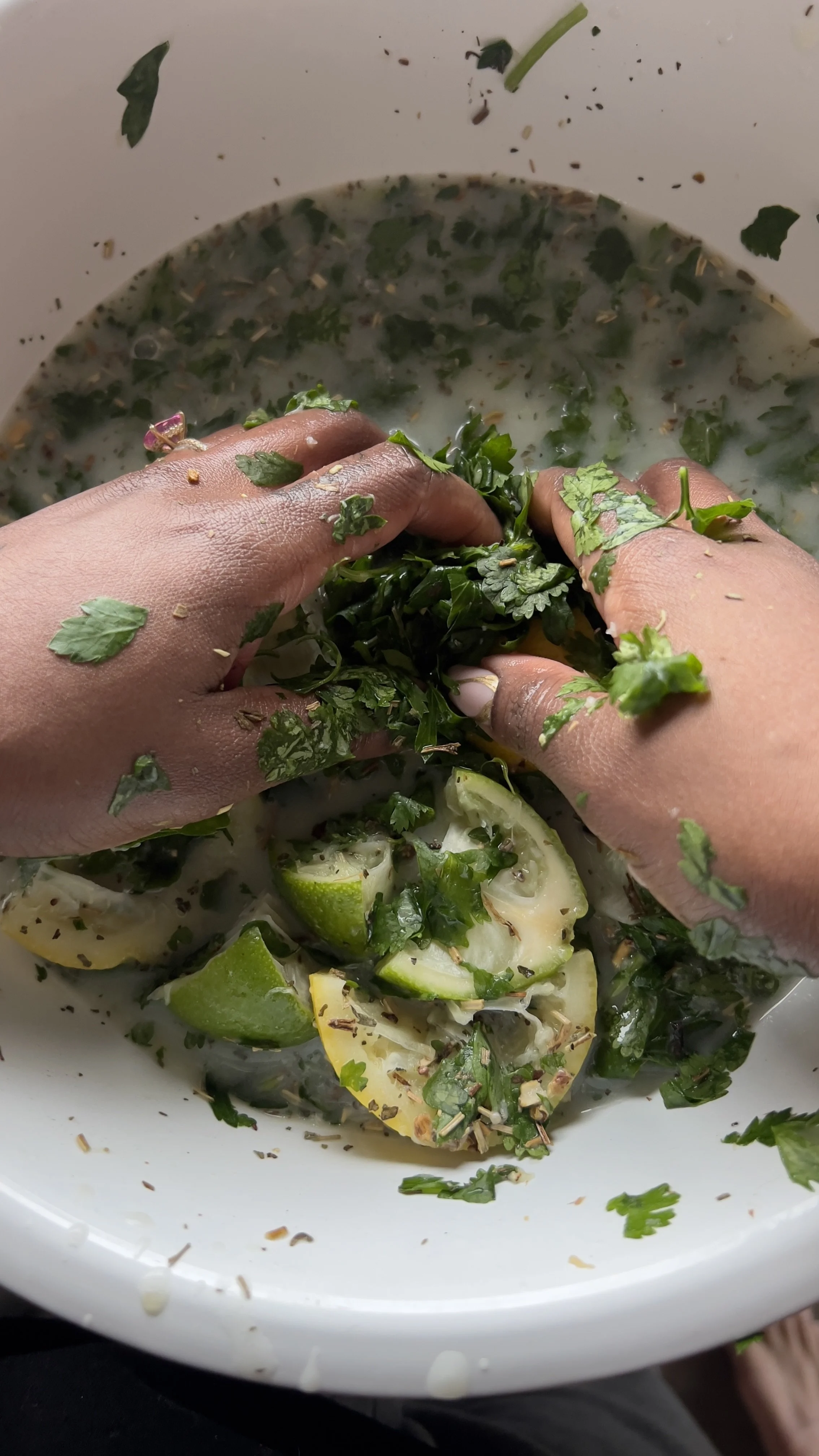 Multiple hands chopping fresh cilantro, lime wedges, and green herbs in a bowl, with some herbs spilling over the sides.