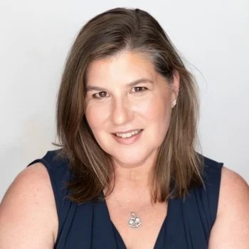 Dr. Kristina Berger, a woman with shoulder-length brown hair, smiling, wearing a navy sleeveless top and a necklace with a butterfly pendant, against a white background.